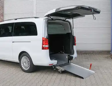 Rear side view of a white wheelchair-accessible Mercedes-Benz Vito van with its tailgate open and a fold-out access ramp deployed to the ground.